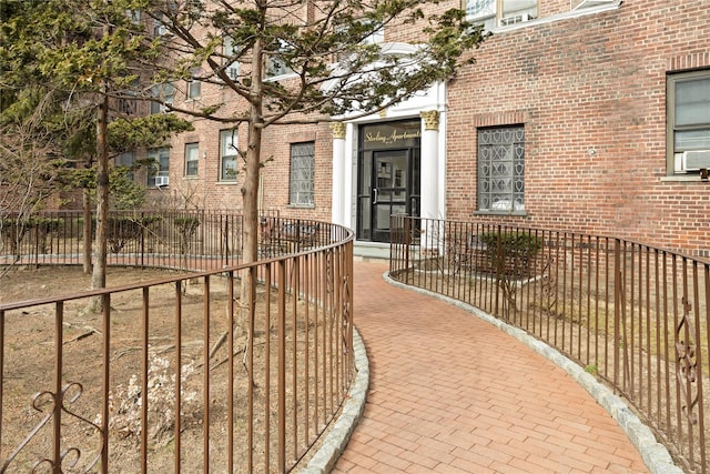 view of exterior entry featuring brick siding and fence