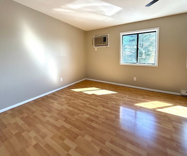 spare room featuring an AC wall unit, light wood finished floors, and baseboards