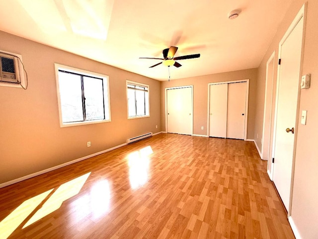 unfurnished bedroom with baseboards, a ceiling fan, a baseboard radiator, light wood-style floors, and two closets