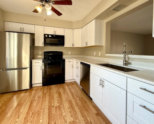 kitchen with light wood finished floors, visible vents, white cabinets, black appliances, and a sink