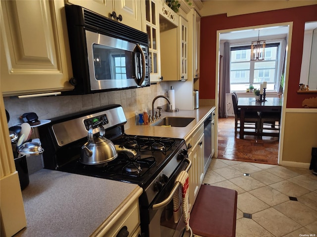 kitchen with appliances with stainless steel finishes, glass insert cabinets, cream cabinets, light countertops, and pendant lighting