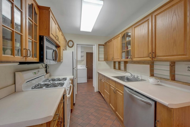 kitchen featuring a sink, light countertops, appliances with stainless steel finishes, washer / clothes dryer, and glass insert cabinets