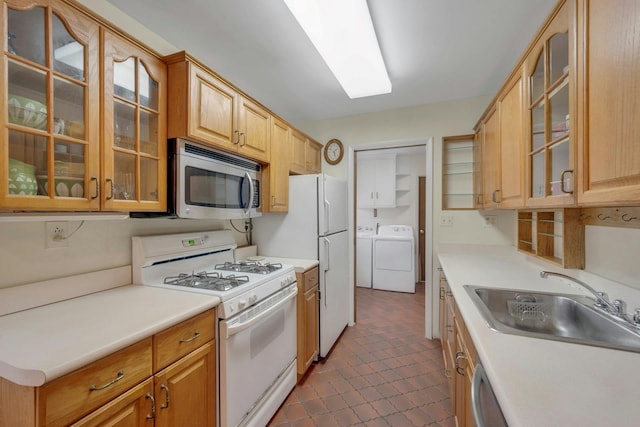 kitchen featuring washing machine and dryer, white appliances, a sink, light countertops, and glass insert cabinets