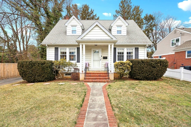 cape cod house with roof with shingles, fence, and a front lawn