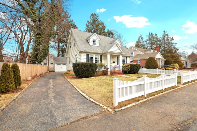 new england style home featuring driveway, a fenced front yard, a chimney, an outbuilding, and a front lawn