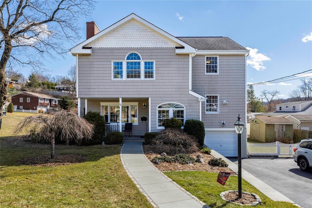 view of front of home with a front lawn, aphalt driveway, a porch, a garage, and a chimney