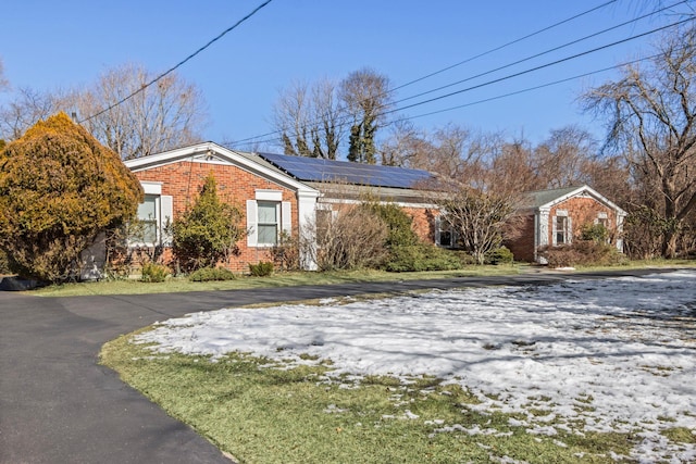 view of front of property with roof mounted solar panels, brick siding, and driveway