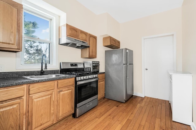 kitchen featuring under cabinet range hood, a sink, appliances with stainless steel finishes, light wood finished floors, and dark countertops