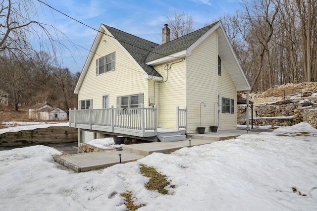 snow covered property with a deck, roof with shingles, a chimney, and a garage