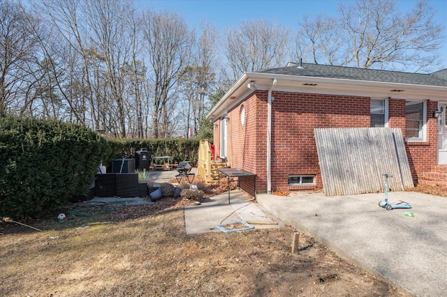 view of side of property with a patio area, roof with shingles, and brick siding