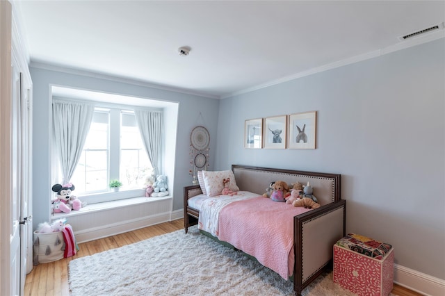 bedroom with baseboards, visible vents, wood finished floors, and ornamental molding