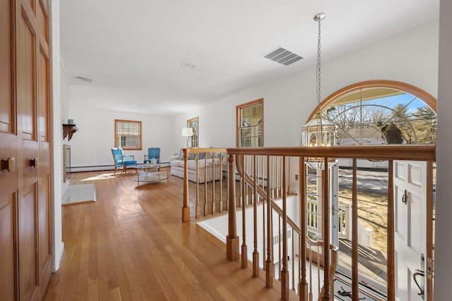 hallway featuring a baseboard radiator, visible vents, light wood-style flooring, and an upstairs landing