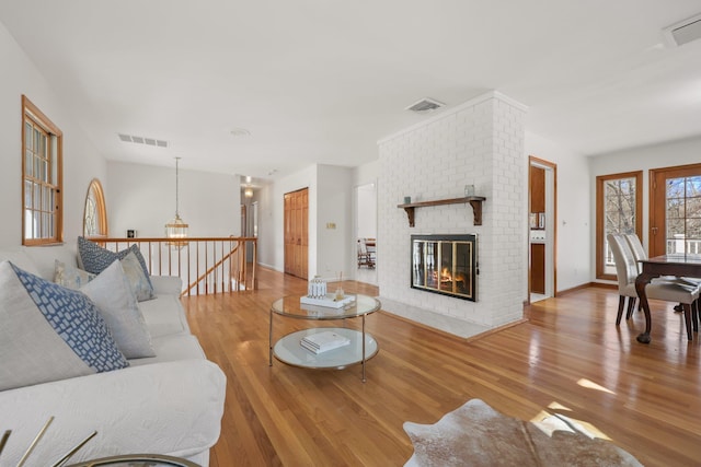 living room with a brick fireplace, visible vents, and wood finished floors