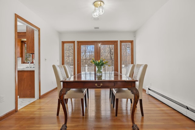 dining room featuring a baseboard heating unit, baseboards, visible vents, and light wood finished floors