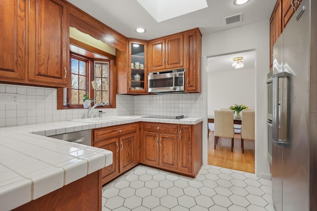 kitchen with tile counters, appliances with stainless steel finishes, brown cabinetry, and visible vents