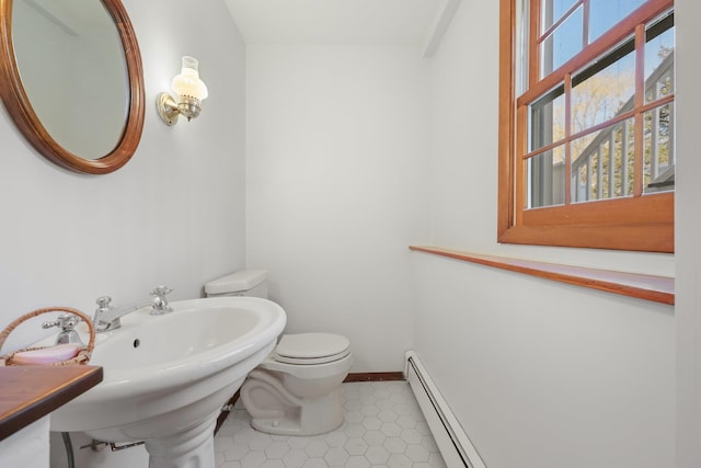 half bathroom featuring toilet, a baseboard heating unit, a sink, baseboards, and tile patterned floors