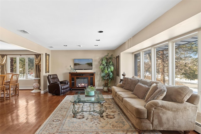 living area featuring wood finished floors, a glass covered fireplace, visible vents, and baseboards