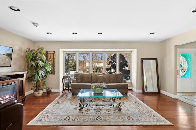 living room featuring baseboards, dark wood finished floors, and a glass covered fireplace