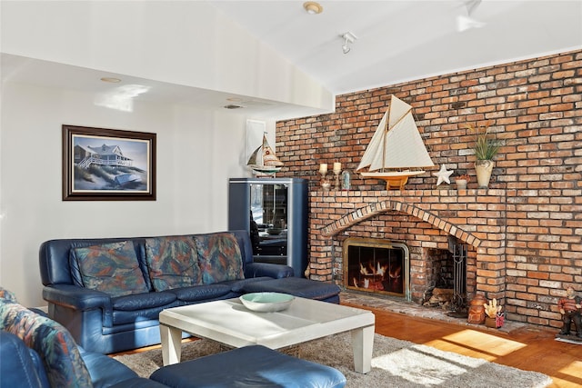 living room featuring a brick fireplace, vaulted ceiling, and wood finished floors