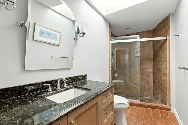 bathroom featuring a skylight, toilet, wood tiled floor, a shower stall, and vanity