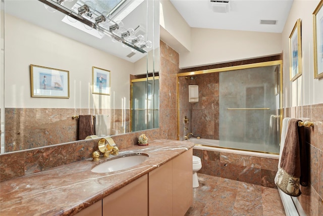 bathroom featuring visible vents, toilet, tiled shower / bath, vanity, and tile walls