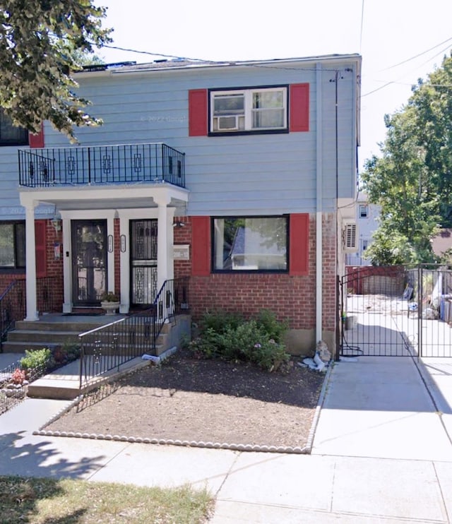 view of front of home featuring a balcony, a gate, fence, and brick siding