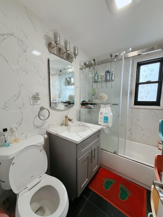 bathroom featuring toilet, vanity, tile walls, combined bath / shower with glass door, and tile patterned floors