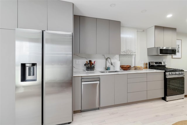 kitchen featuring stainless steel appliances, light countertops, gray cabinetry, a sink, and modern cabinets