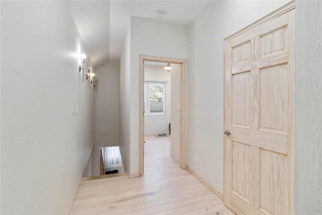 corridor with light wood-style flooring, baseboards, and vaulted ceiling