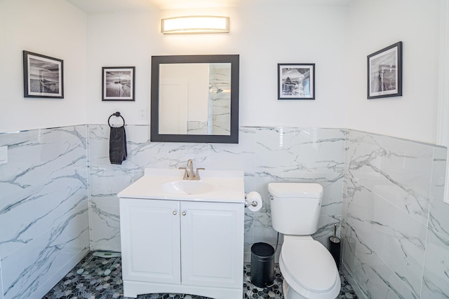 bathroom featuring tile walls, wainscoting, vanity, and toilet