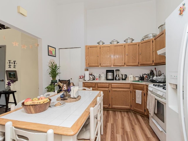 kitchen featuring white appliances, tile countertops, a high ceiling, light wood-type flooring, and under cabinet range hood