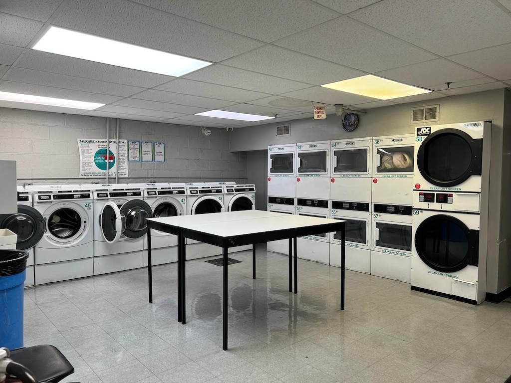 common laundry area featuring concrete block wall, washing machine and dryer, visible vents, and stacked washer / drying machine