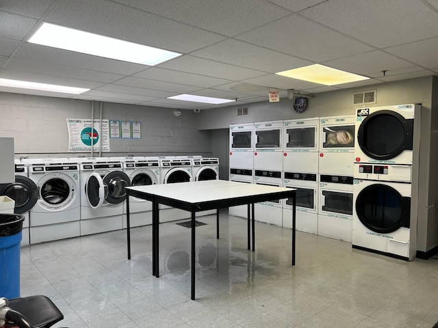 common laundry area featuring concrete block wall, washing machine and dryer, visible vents, and stacked washer / drying machine