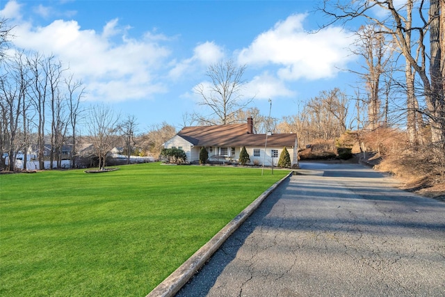 view of front of home with a front lawn, a chimney, and aphalt driveway