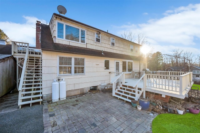 rear view of property with a chimney, roof with shingles, stairs, a deck, and a patio area