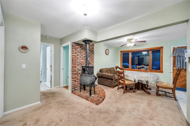 living area featuring a wood stove, ceiling fan, baseboards, and light colored carpet