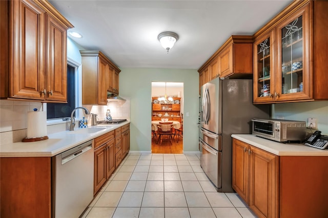 kitchen with glass insert cabinets, brown cabinets, stainless steel appliances, light countertops, and a sink