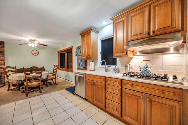 kitchen with appliances with stainless steel finishes, light countertops, under cabinet range hood, a sink, and light tile patterned flooring