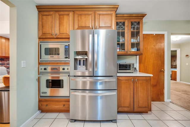 kitchen with appliances with stainless steel finishes, brown cabinets, light countertops, and glass insert cabinets