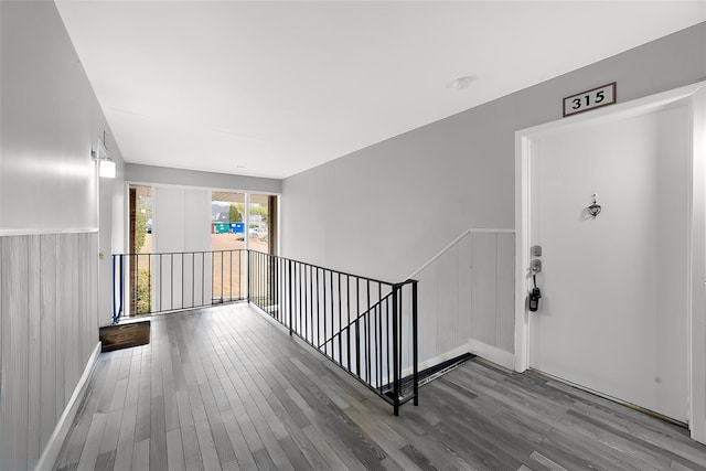 hall with a wainscoted wall, wood finished floors, and an upstairs landing