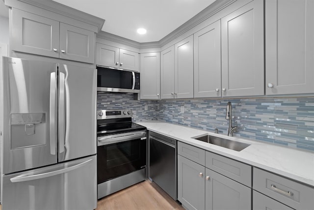 kitchen featuring light wood finished floors, stainless steel appliances, decorative backsplash, gray cabinetry, and a sink