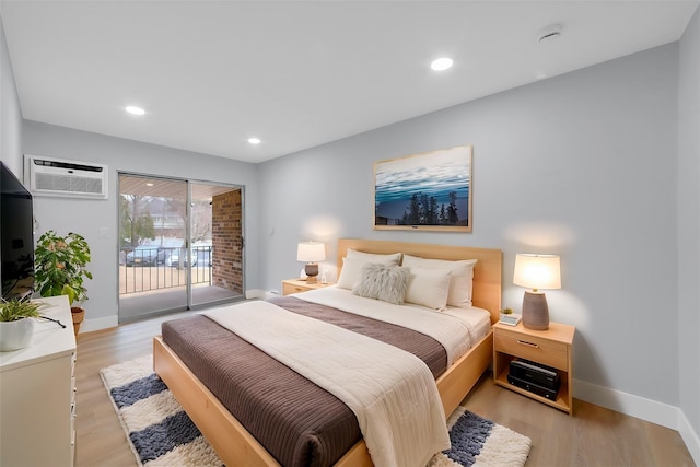 bedroom featuring baseboards, light wood finished floors, a wall unit AC, and access to exterior