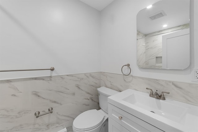 bathroom with toilet, vanity, visible vents, tile walls, and wainscoting