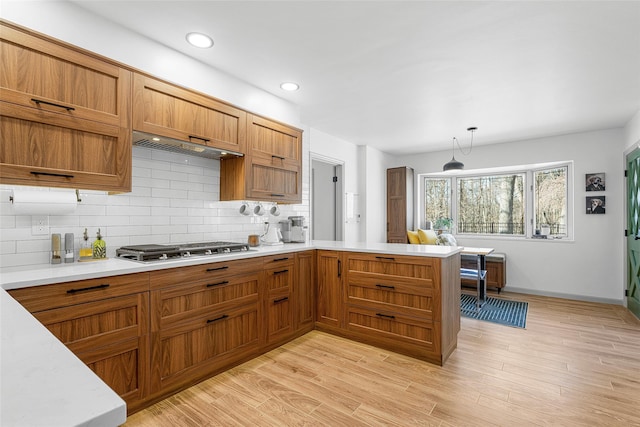 kitchen with light wood-type flooring, a peninsula, light countertops, decorative backsplash, and stainless steel gas cooktop