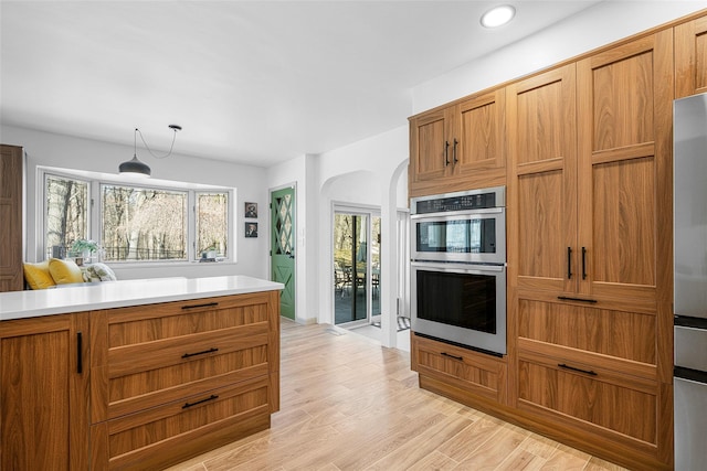 kitchen with brown cabinets, stainless steel appliances, arched walkways, light wood-style floors, and light countertops