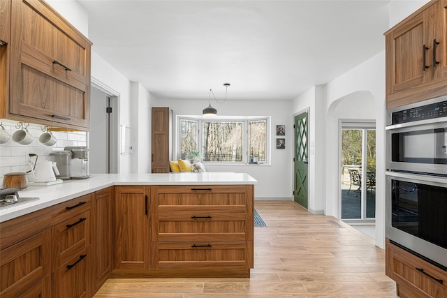 kitchen with a healthy amount of sunlight, a peninsula, light wood-style flooring, double oven, and tasteful backsplash