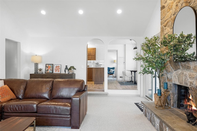 living room featuring light colored carpet, recessed lighting, a fireplace, and arched walkways