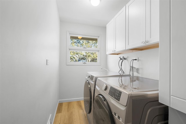 laundry area featuring washing machine and dryer, cabinet space, baseboards, and light wood finished floors