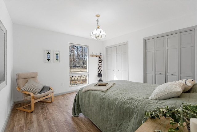 bedroom featuring a notable chandelier, baseboards, multiple closets, and wood finished floors