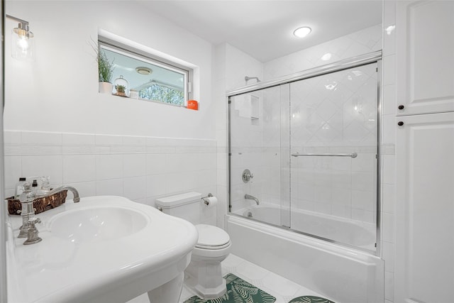 full bathroom with a wainscoted wall, toilet, shower / bath combination with glass door, tile patterned floors, and tile walls